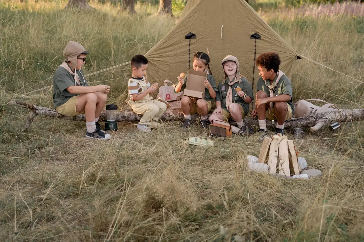 Kinder sitzen im Feriencamp vor einem Zelt im Gras
